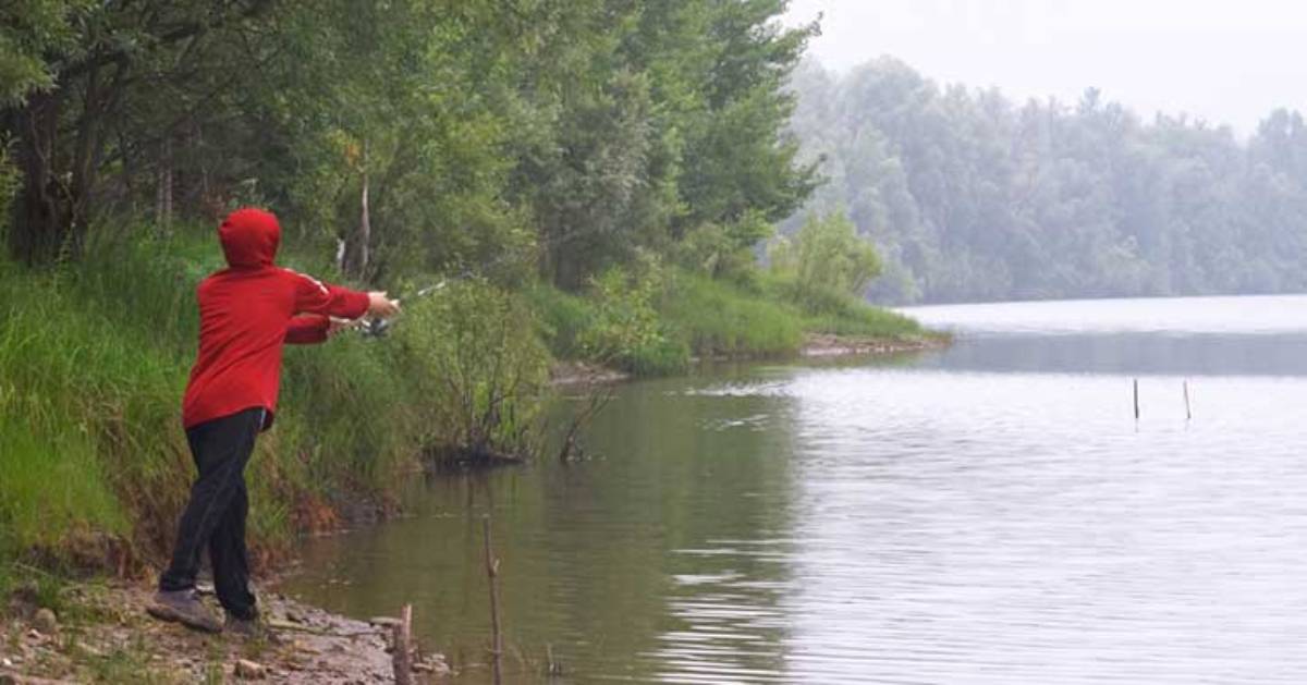 person with red sweater casting fishing line from shore