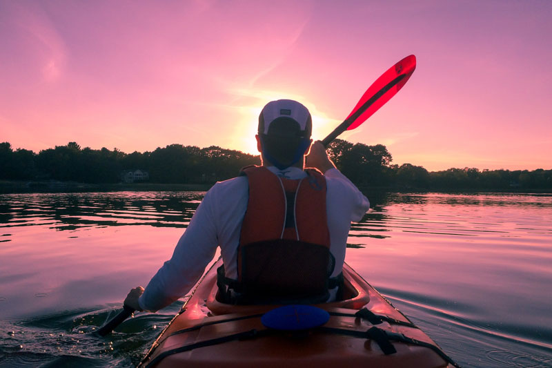 man kayaking on lake with sunset above