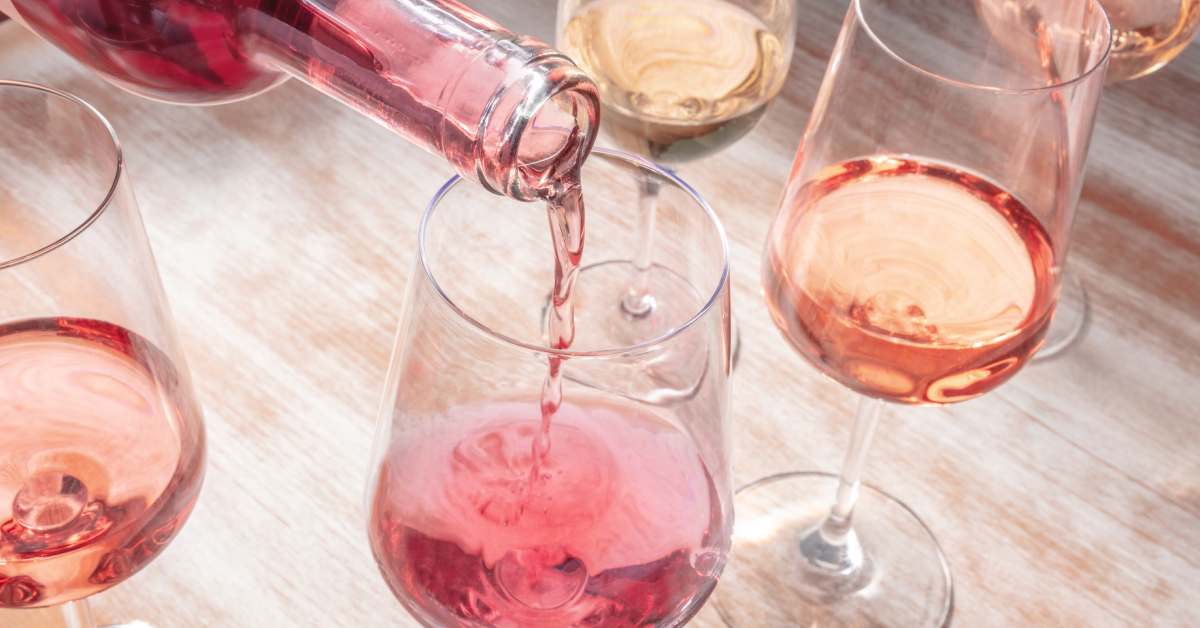 wine glasses on table, rose wine being poured into one