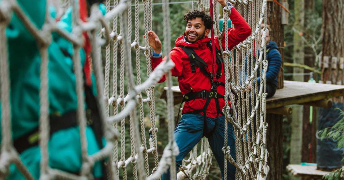 man climbing along rope nets in a treetop course