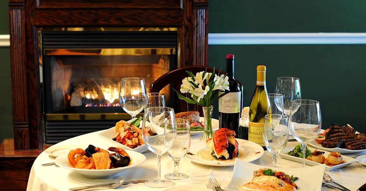 table with food and glasses on it in front of a fireplace