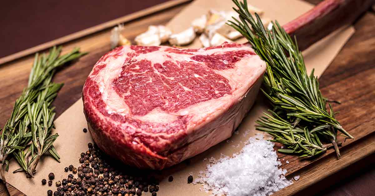 raw steak on a cutting board with rosemary, salt, and pepper