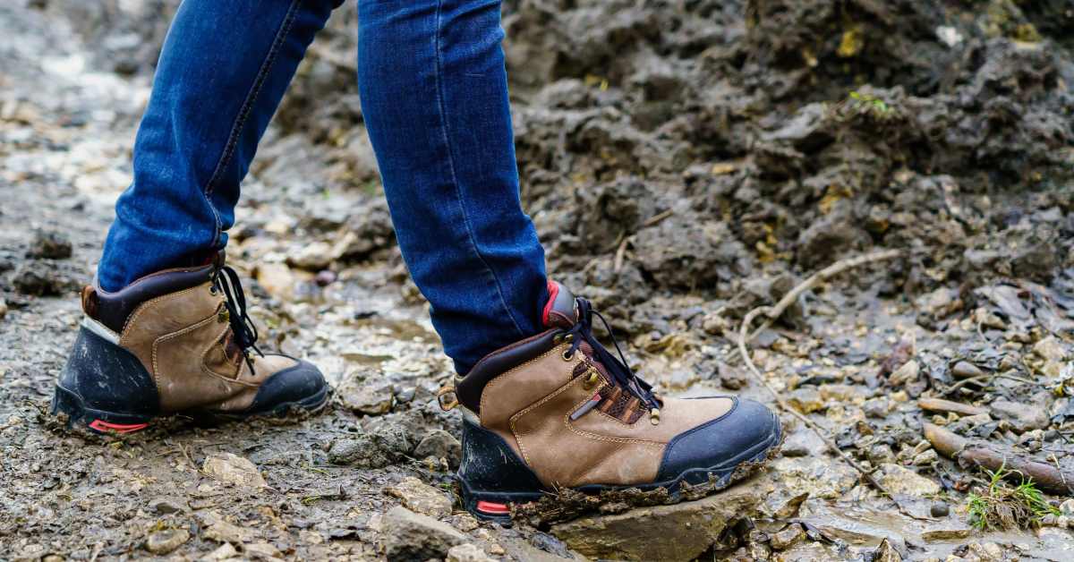 person wearing blue jeans and hiking boots walking on muddy trail