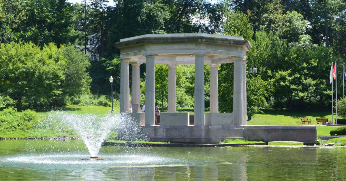 a pond, fountain, and memorial in the lush green landscape of Congress Park