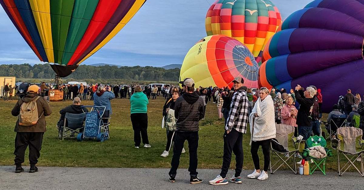 people at a hot air balloon festival, balloons are just being blown up to take off