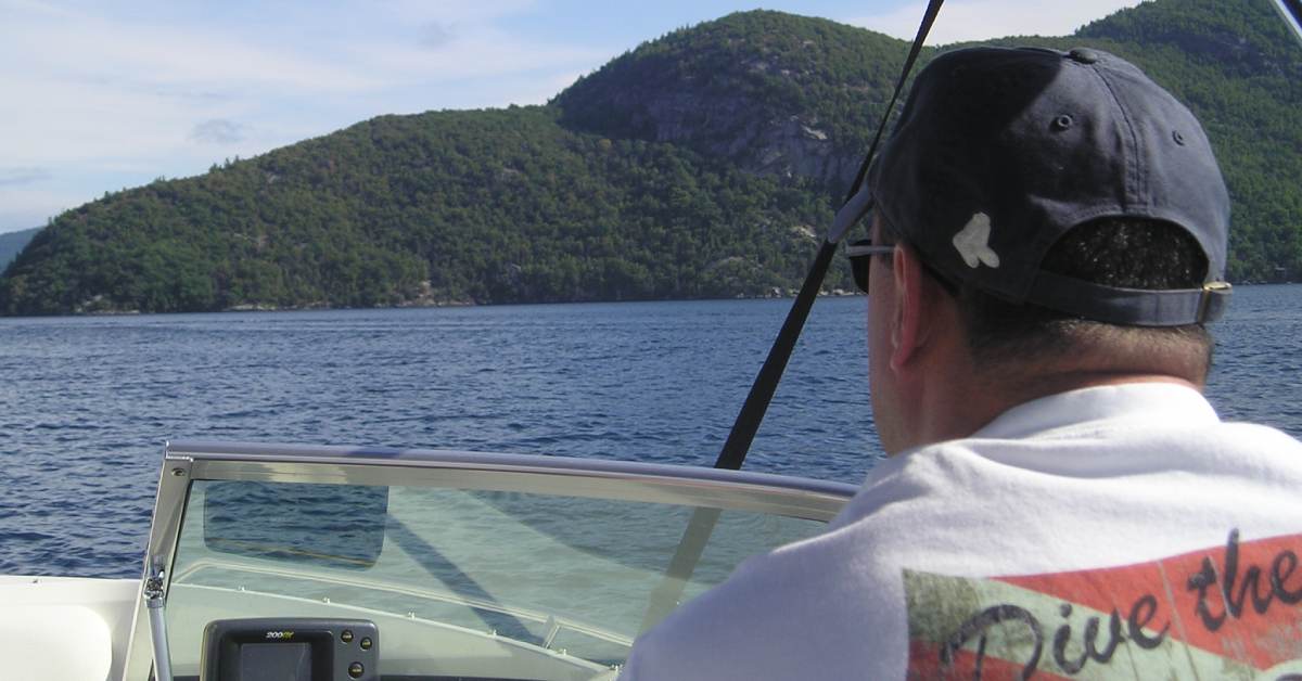 a man with a hat and t shirt driving a boat on a lake