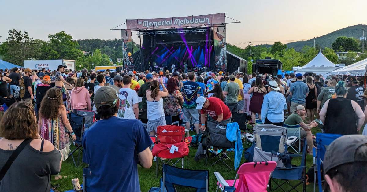 crowd at an outdoor music event, stage with sign memorial meltdown