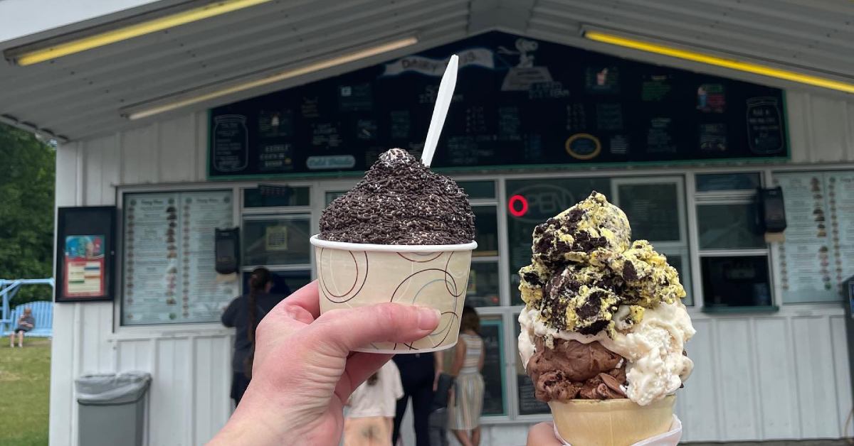 two people holding up icecream in front of an ice cream store