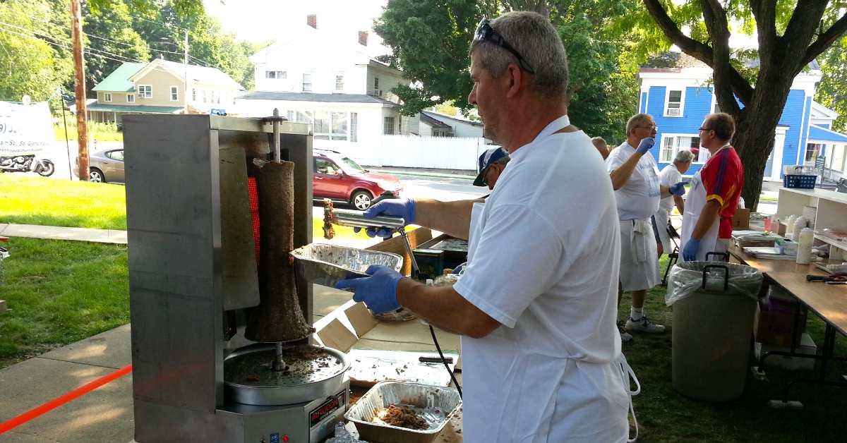 man cutting meat at an outdoor food festival table