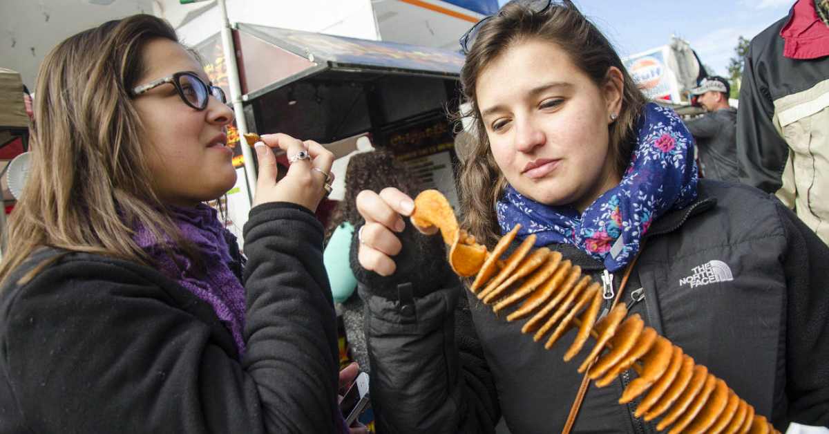 two women eating snacks from a long skewer