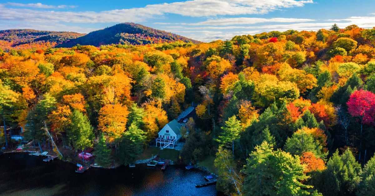 aerial view of a house on a lake with fall colored trees surrounding it