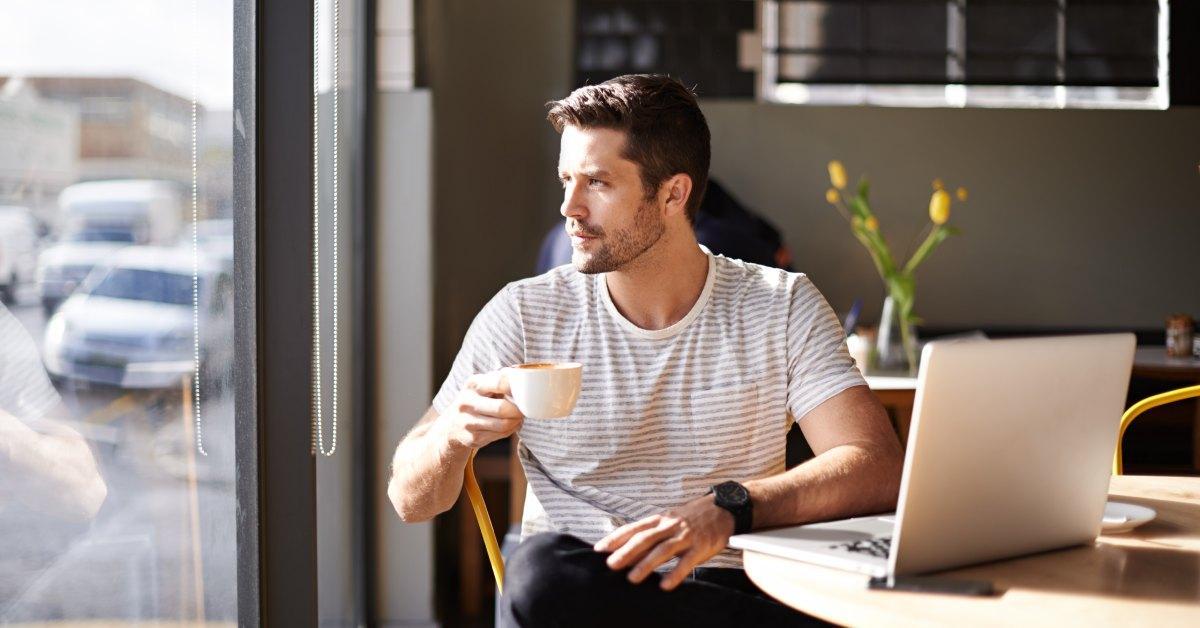 man drinking coffee while sitting at a desk looking outside