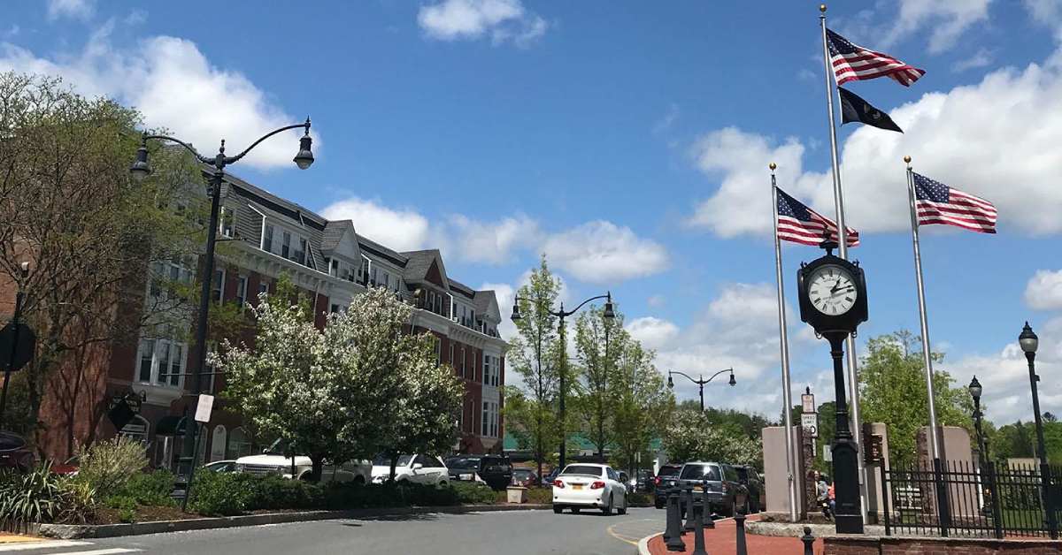 a street with a building on the left and a clock and flags on the right