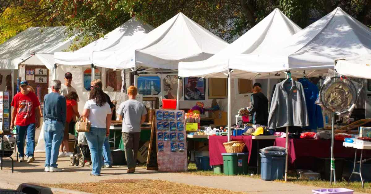 people walking along a sidewalk past tents with products for sale