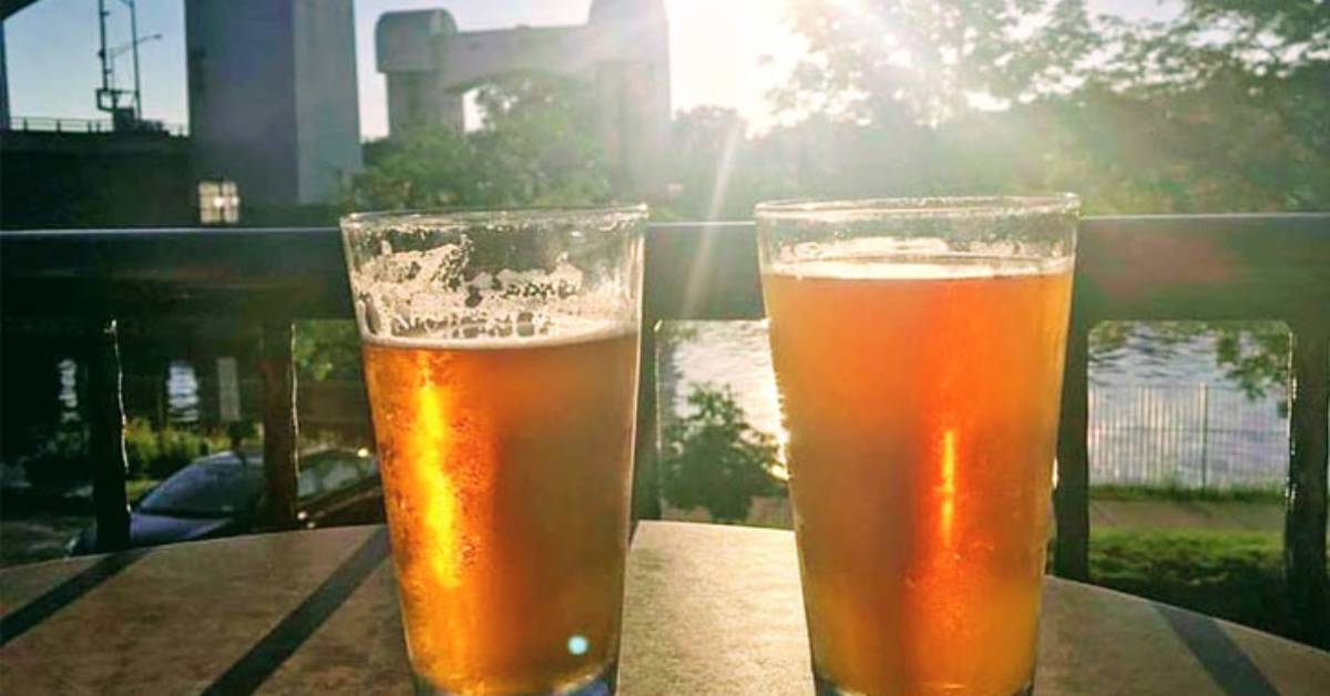 two glasses of beer on a table with water in the background