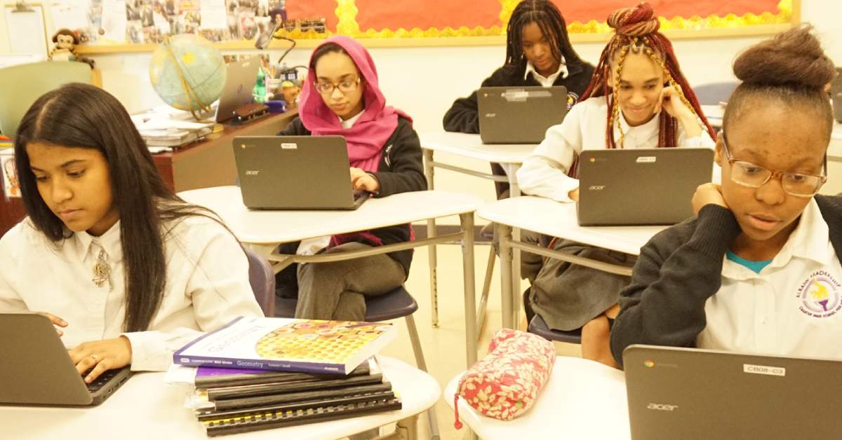 five female students at their desks with laptops