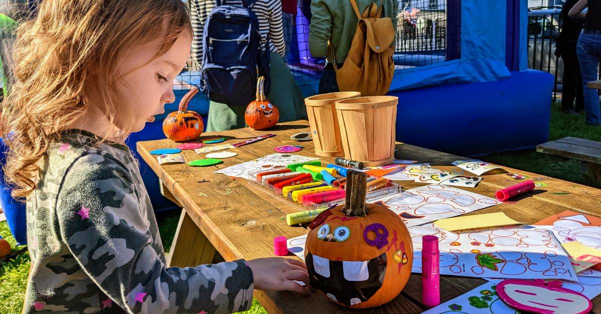 little girl at picnic table at outdoor event decorates a pumpkin