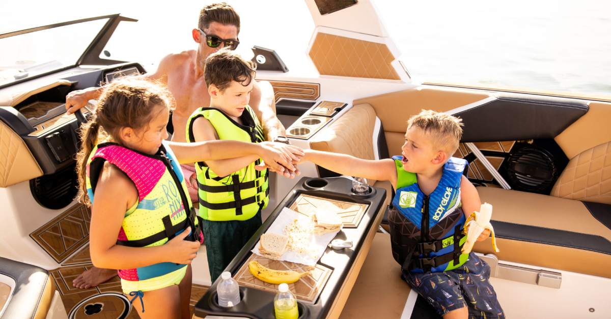 three kids and an adult with lifejackets on eating lunch on a boat