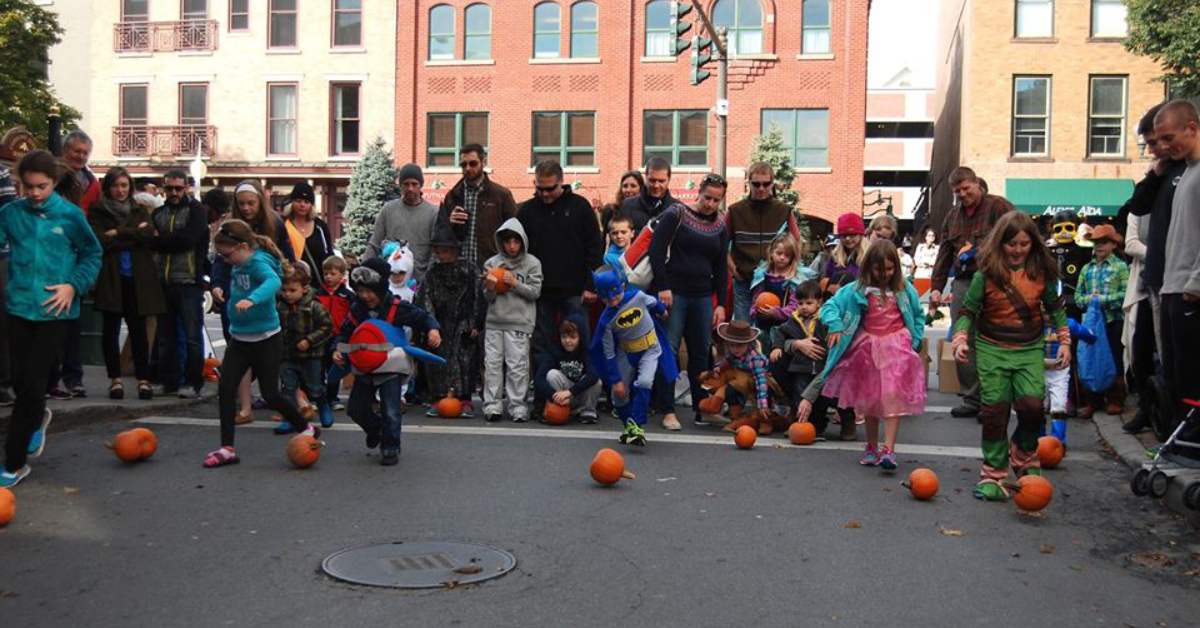 kids in halloween costumes participating in a pumpkin rolling contest