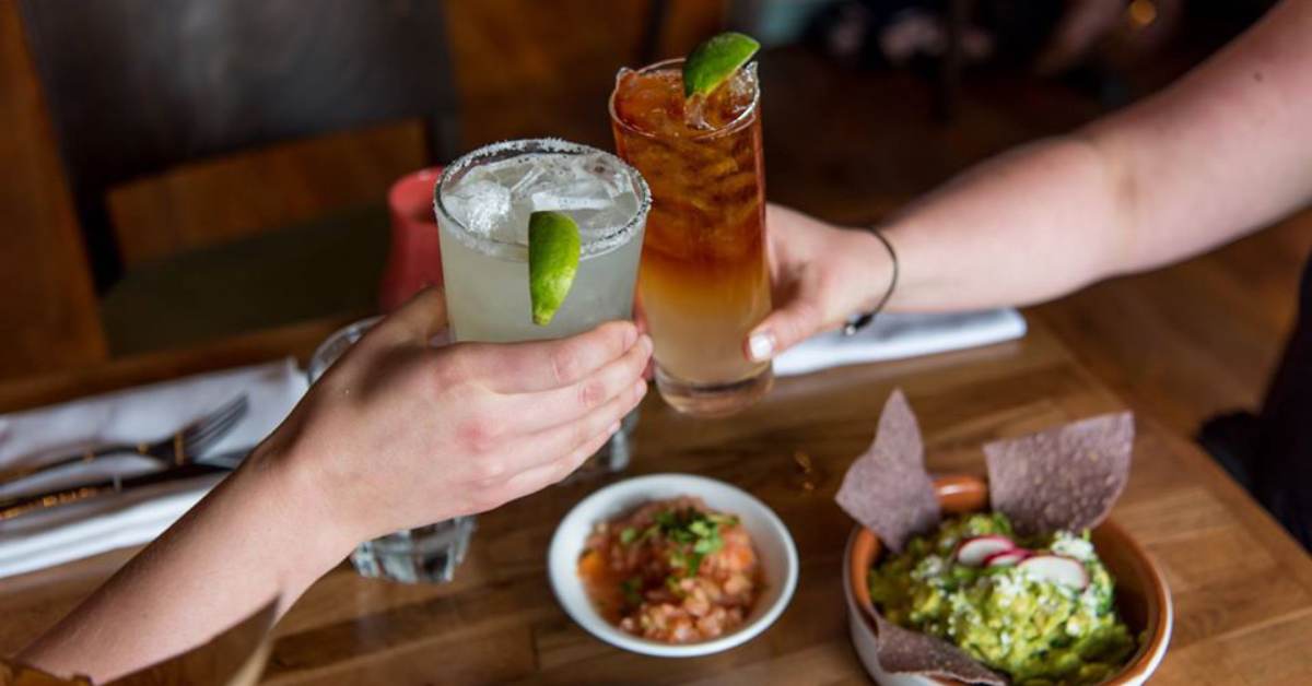 hands with drinks cheersing over table with mexican food