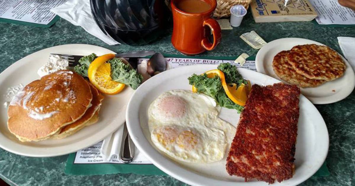 breakfast spread out with pancakes, two eggs, an omelette, two sausages, and coffee