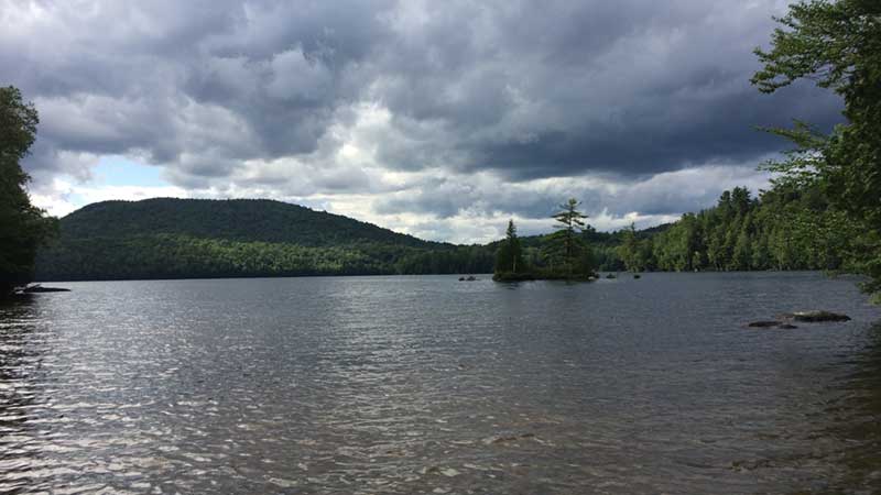 A body of water lined by green trees near Ray Brook NY