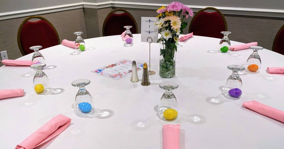 table set for easter with colored eggs under overturned glasses and pink napkins