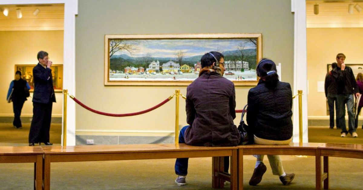 two people sitting on a bench in a museum gallery