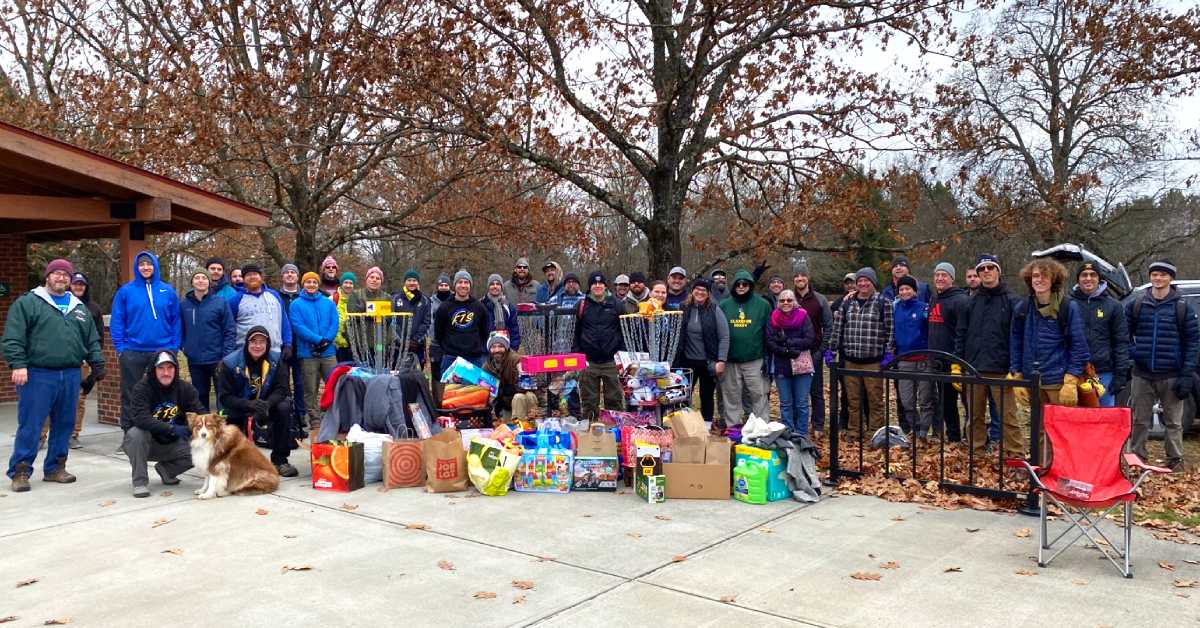 people with donation items by disc golf course baskets