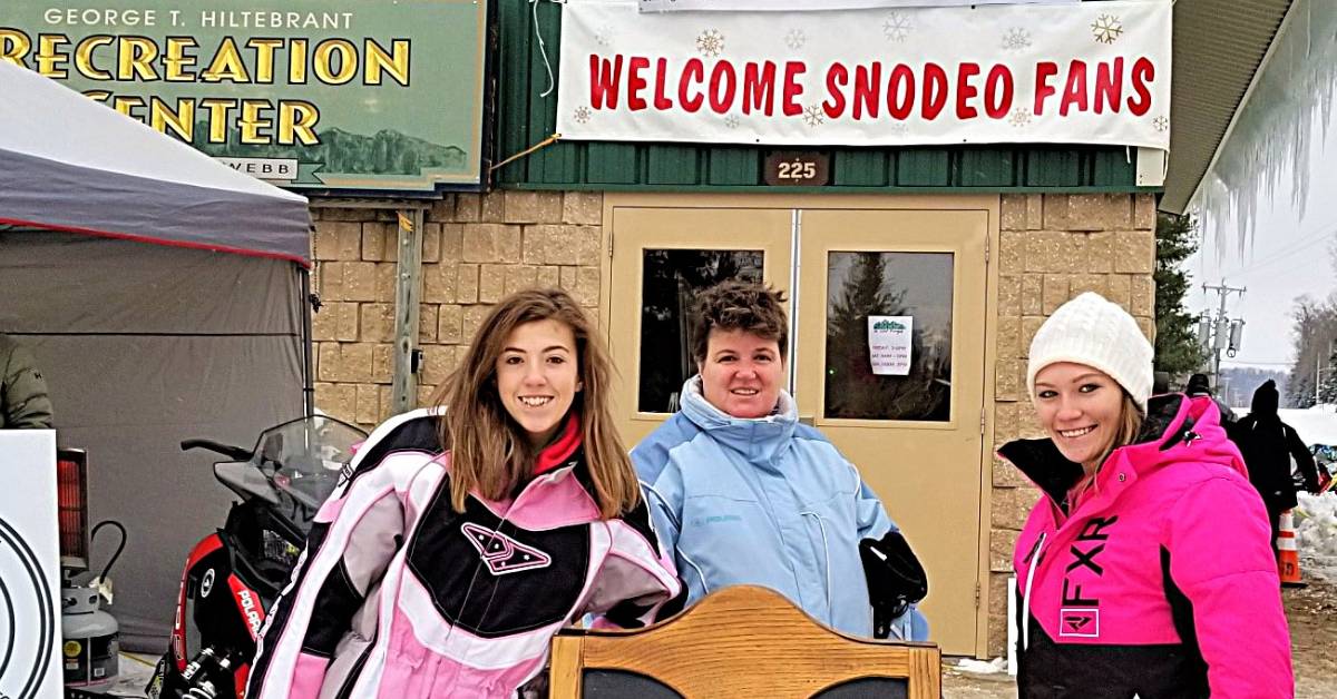 three women pose in front of welcome snodeo fans sign