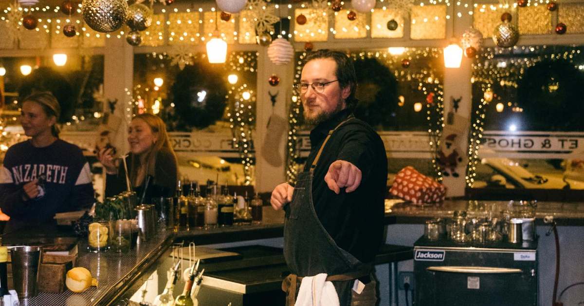 a bartender pointing in a dining area with holiday decor on the ceiling