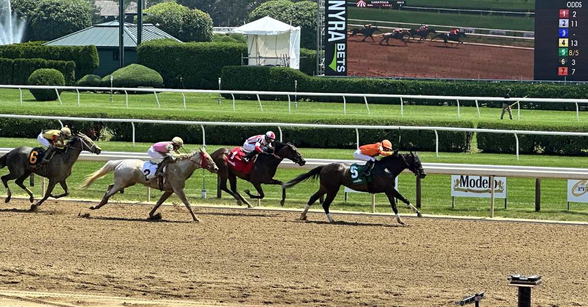 four horses racing on a dirt track