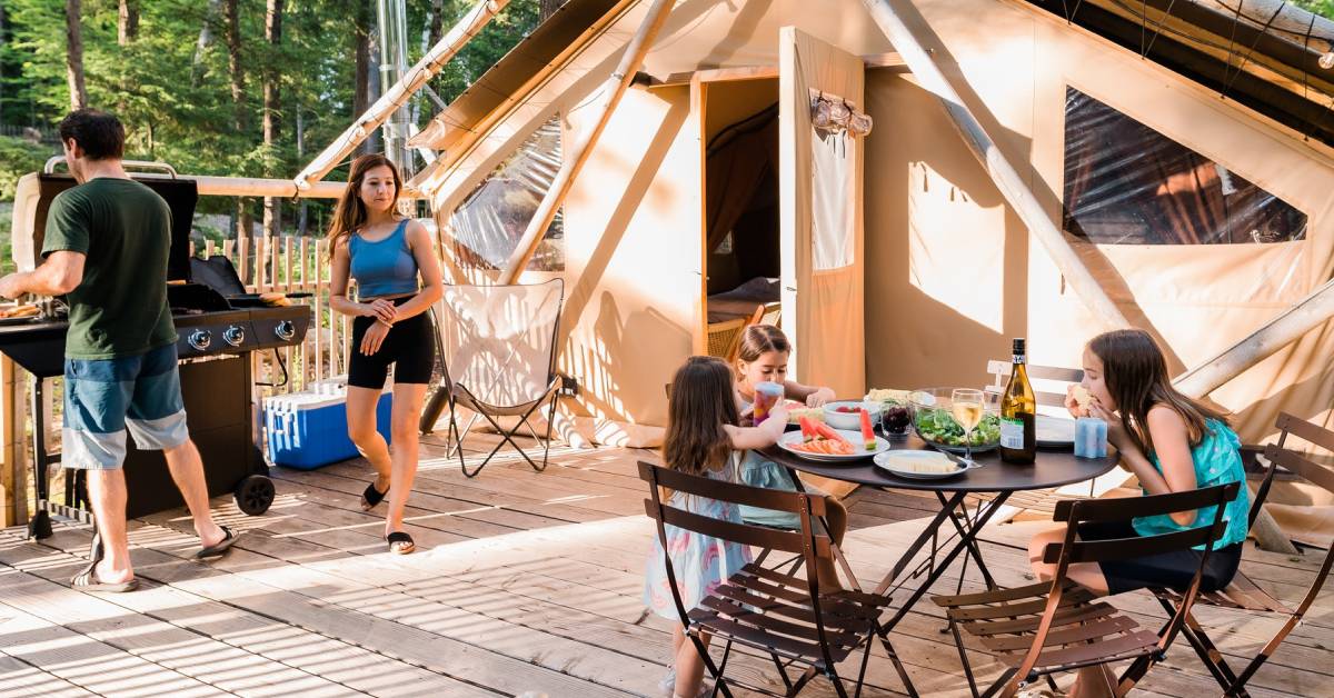 huttopia adirondacks - family grilling and eating outside glamping tent