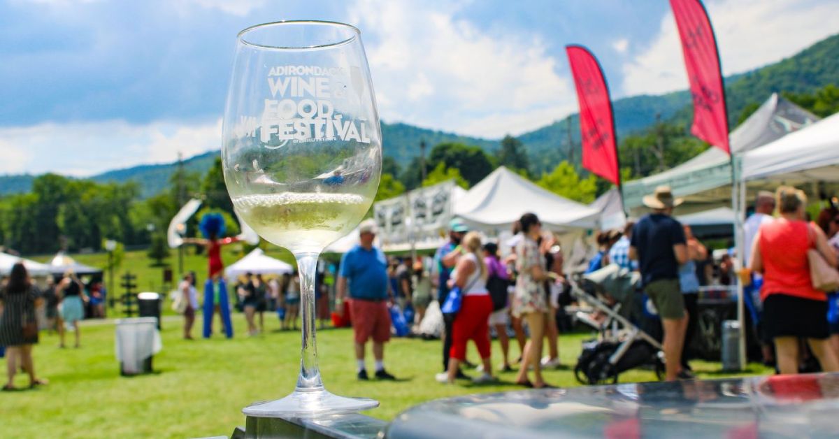 adk wine and food fest glass on a table with view of the festival in the background