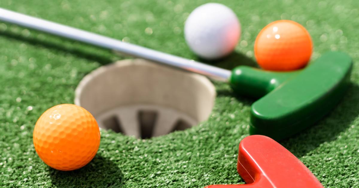 mini golf putters and balls near a hole
