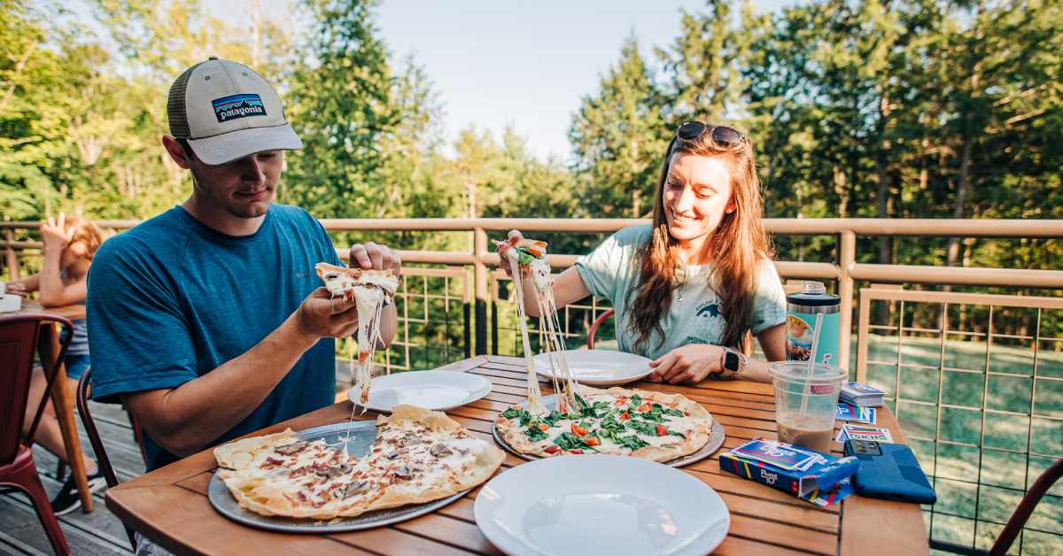 man and woman at an outdoor deck table with pizzas