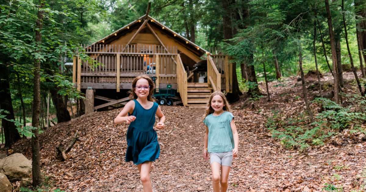 two girls walking away from a glamping tent in the woods