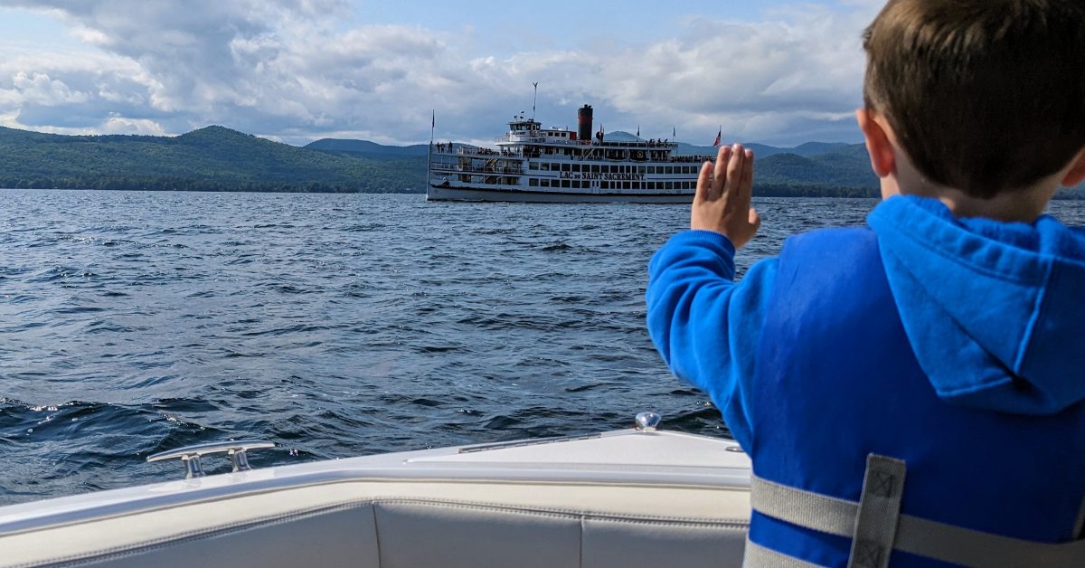 a kid on a boat waves to the lake george steamboat company going by