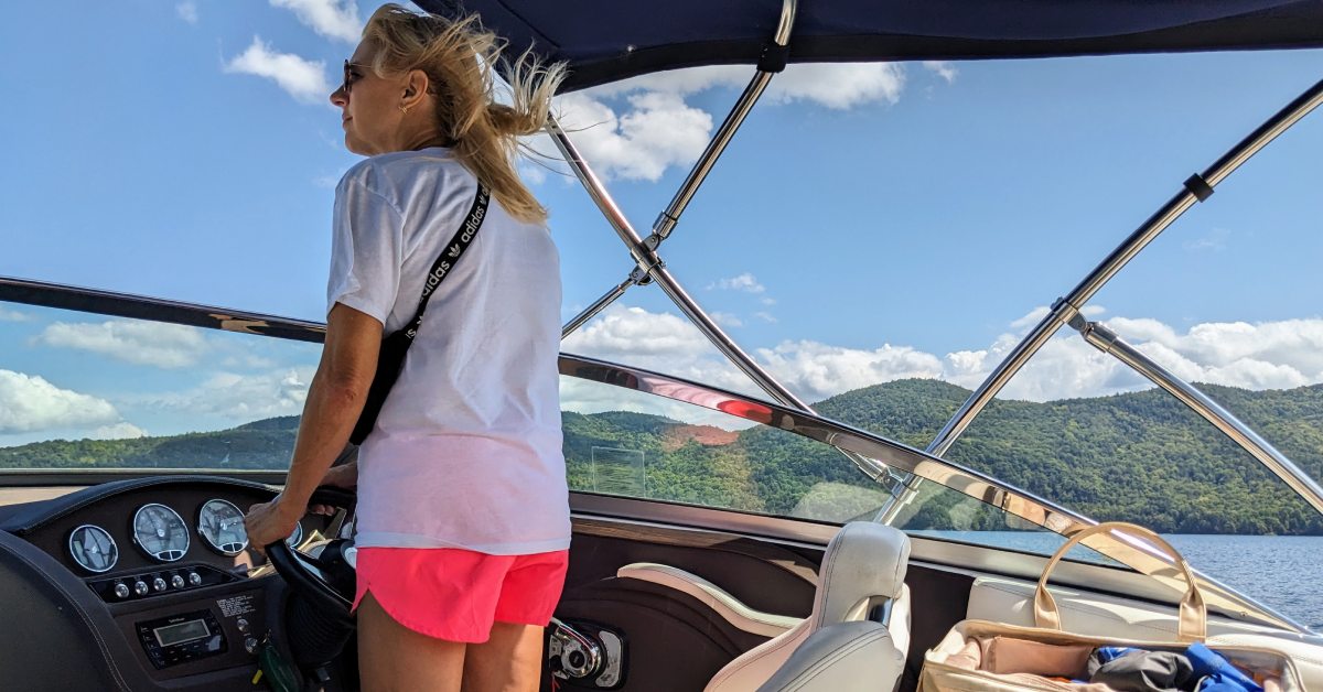 woman on boat drives while looking over windshield