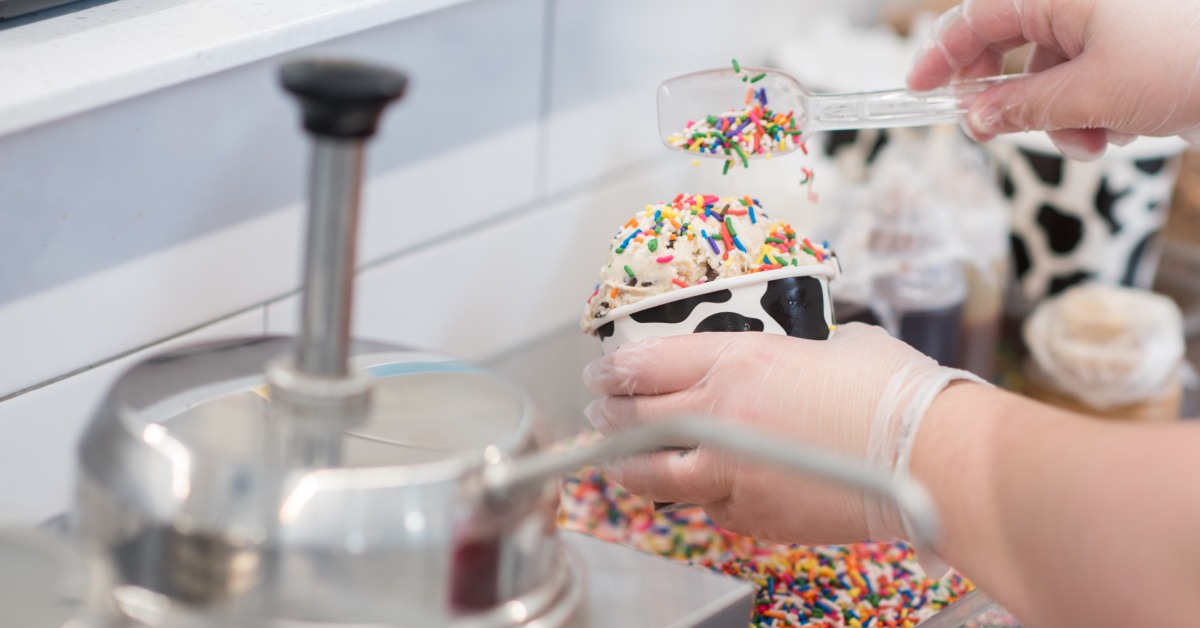 Close up of someone's hands making a dish of ice cream with rainbow sprinkles