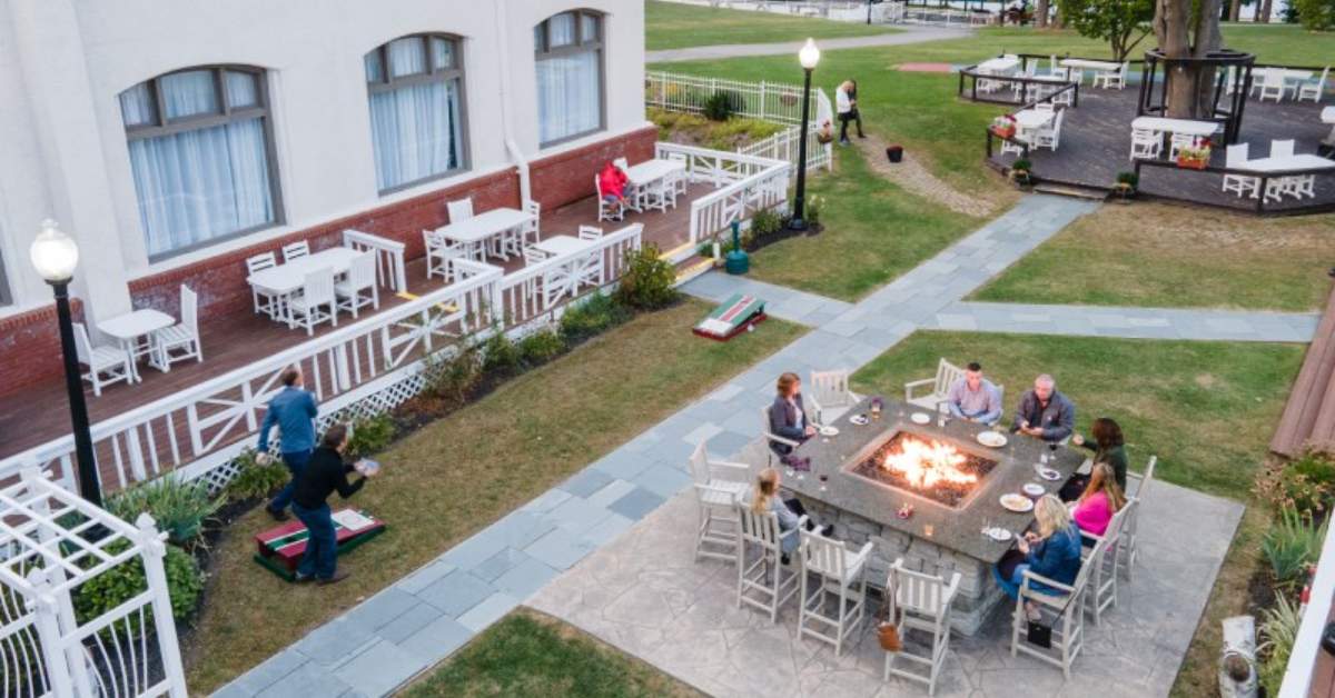 Outdoor patio with people sitting around a fire and others playing cornhole
