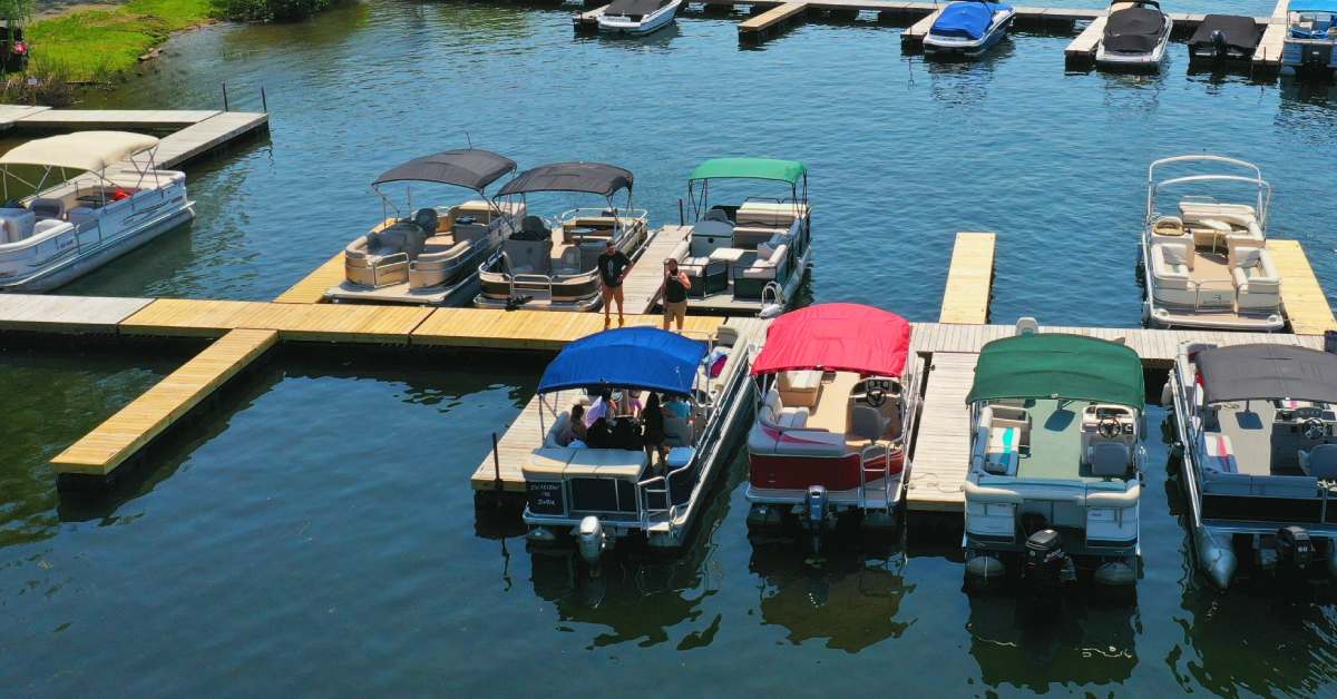 A dock on water that has various pontoon boats parked at it