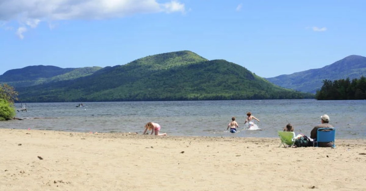 Beach with two people sitting in chairs and 3 people playing in the water