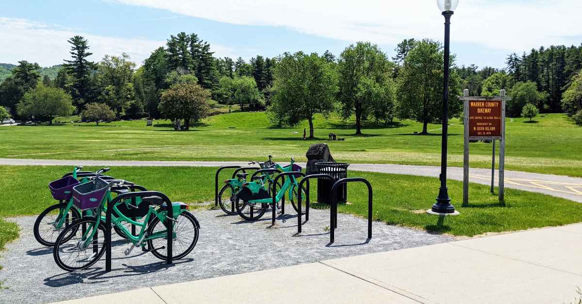 four green bikes in bicycle parking rack by an orange sign for warren county bikeway