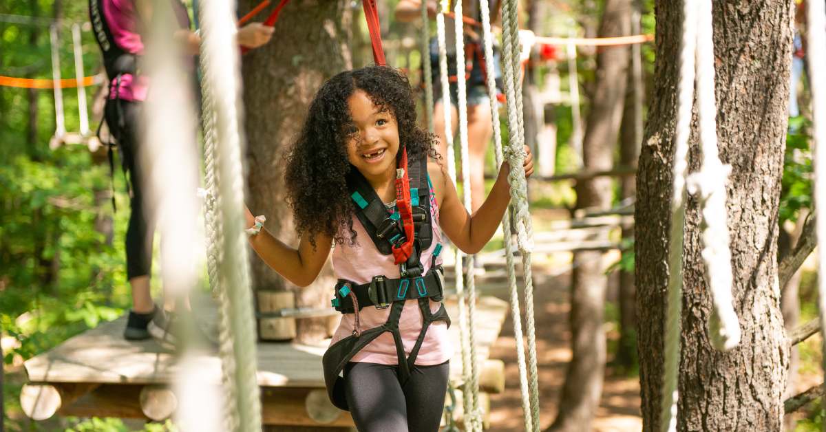 Girl in harness walking on rope bridge 