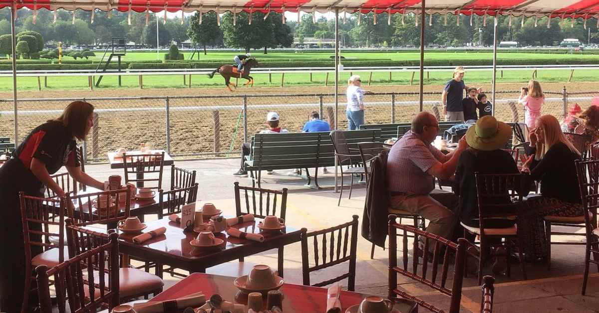 people seated outdoors at tables near a horse race track