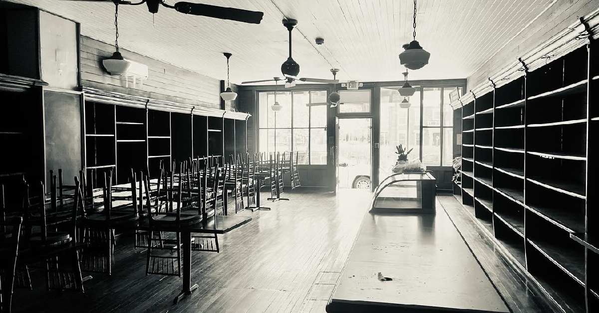 black and white photo of new location with chairs on tables, a counter, and shelving