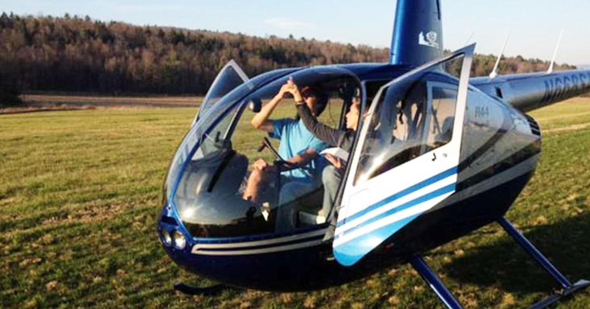 two people sitting in a helicopter on the grass with doors open