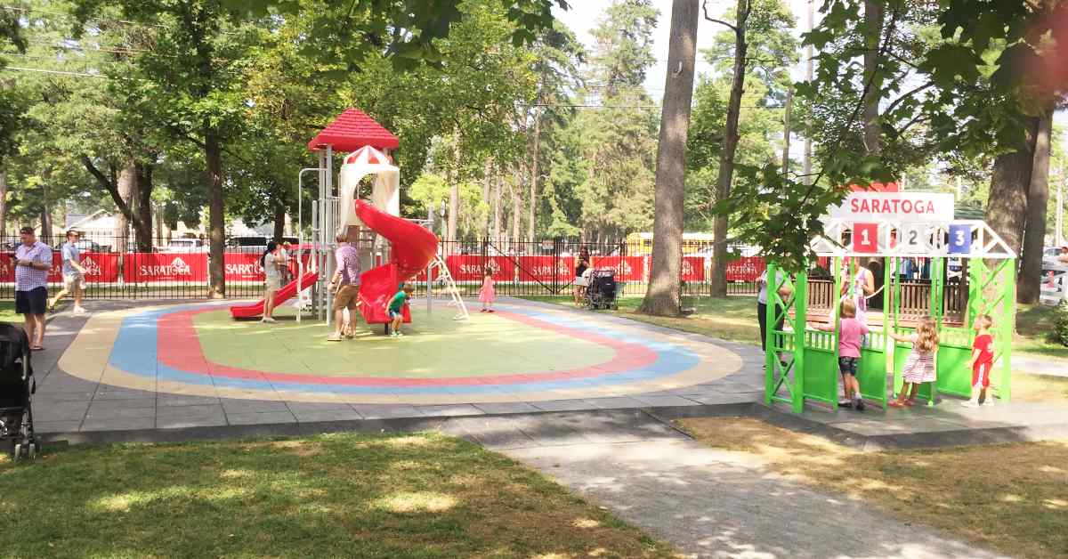 adults and kids at playground in saratoga race track with red slide 