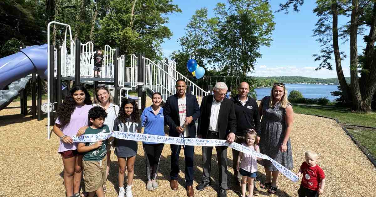 group of people pose in front of new playground holding ribbon